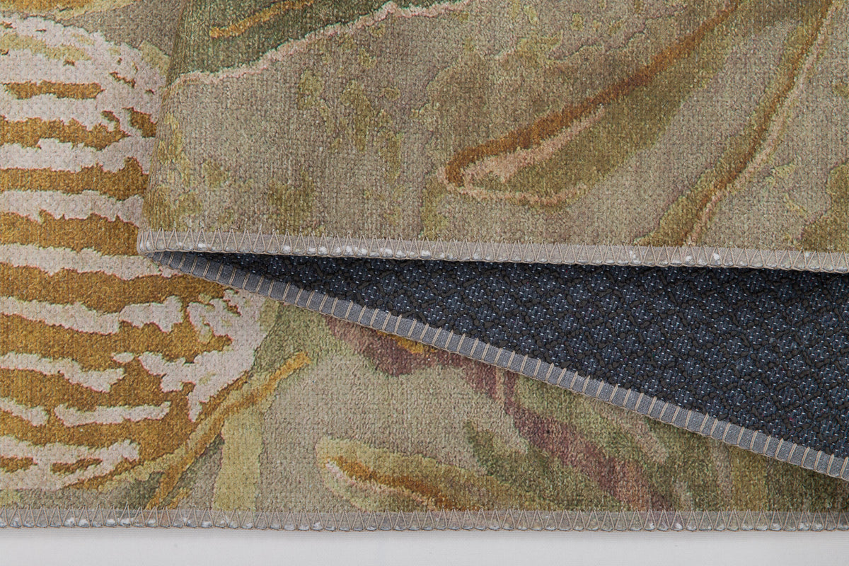 A close-up of Dreamweaver's Loom - Washable Rug - JRS001 shows its abstract beige, brown, and green flat-weave design with a lifted corner revealing the textured black non-slip backing. This washable rug blends style and practicality.