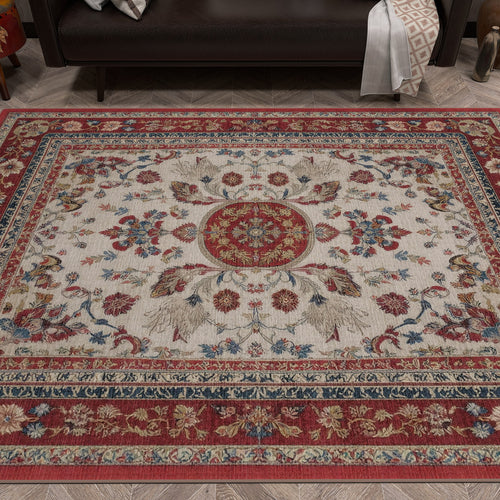 Load image 1 in gallery view. The Imperial Rose - Washable Rug - JRS023, with a red, cream, and blue floral medallion design and ornate borders, is laid on a wooden floor in front of a dark sofa.