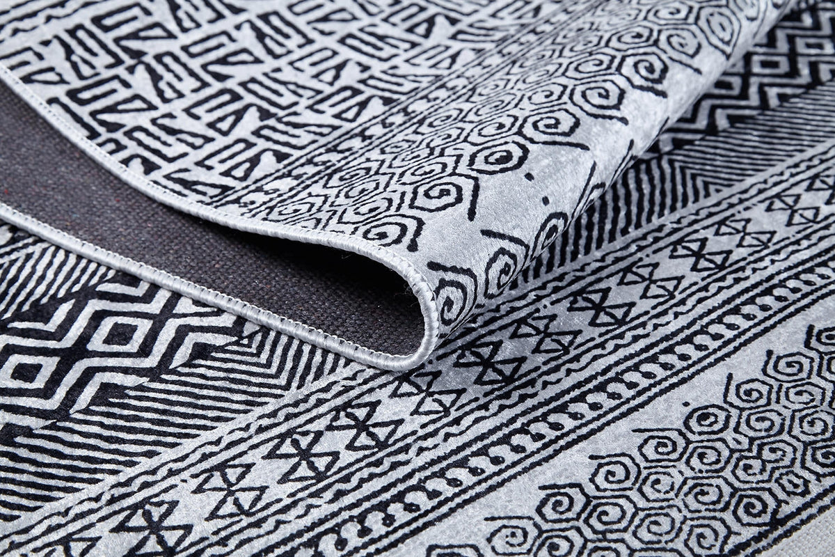 A close-up of the Indie Impressions - Washable Rug - JR1648 (Custom Size) in gray-anthracite, featuring intricate black geometric and spiral designs on a light background, with its edge folded to show both sides of the textile.