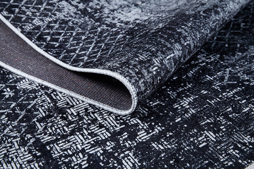 Load image 1 in gallery view. A close-up of the Infinity Garden - Washable Rug - JR1749 (Custom Size), featuring black and white abstract geometric patterns, ideal for high-traffic areas. It’s shown slightly folded to reveal the underside and detailed edge stitching.
