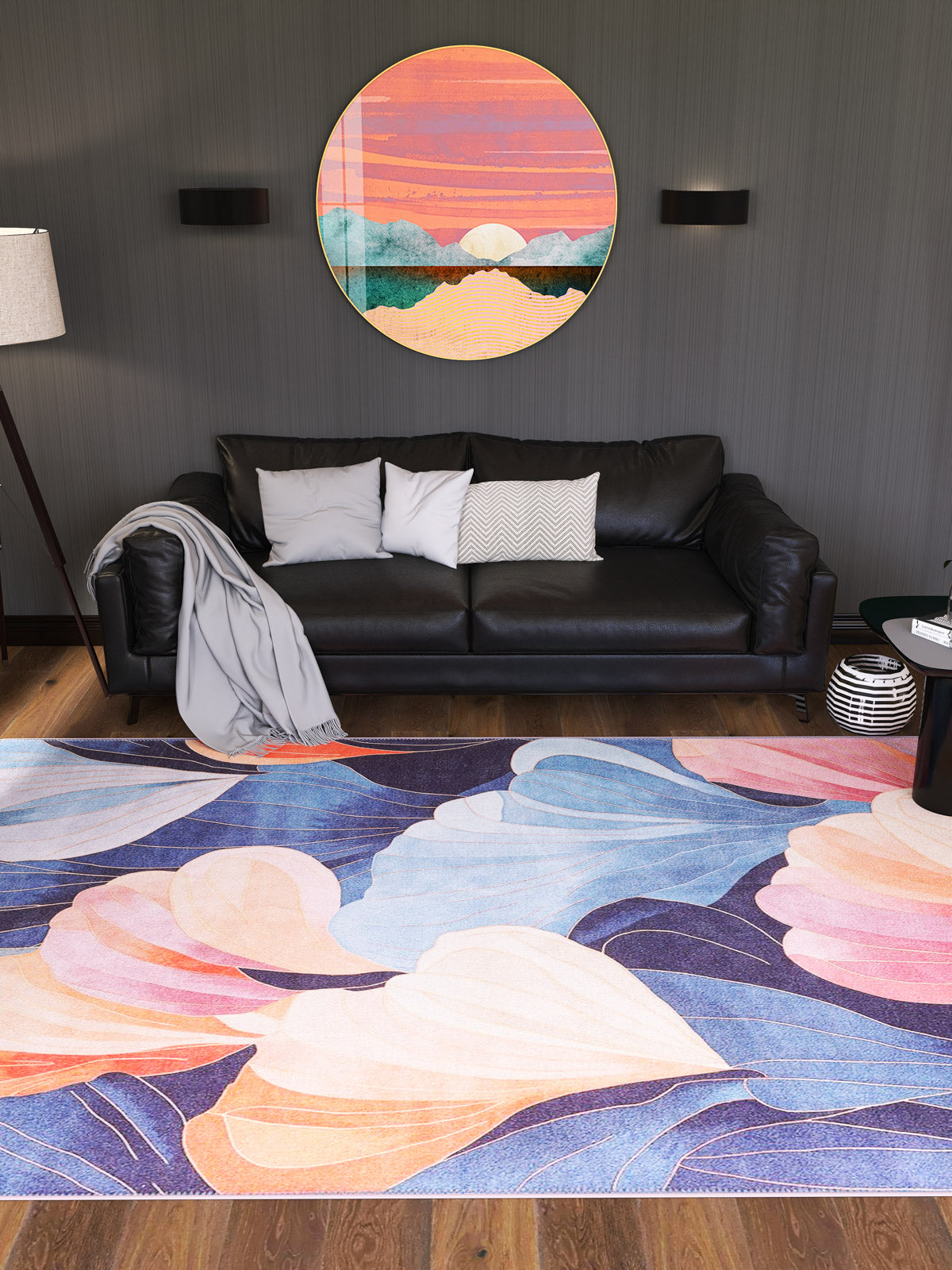 A modern living room with a black sofa, gray and white pillows, light blanket, floor lamp, small side table, round sunset mountain wall art, and the Iris Abstract Floral Washable Rug - MDJ009 in soft pastel tones.