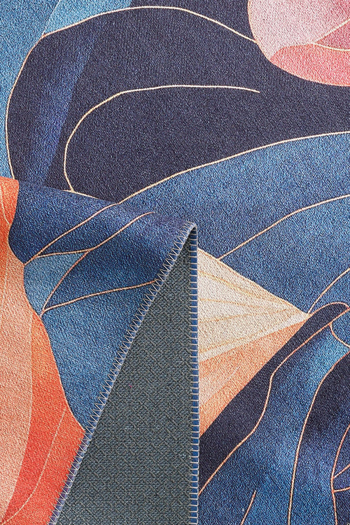 Load image 1 in gallery view. A close-up of the Iris Abstract Floral Washable Rug - MDJ009 shows vibrant blue, orange, pink, and beige abstract shapes. A folded corner reveals its textured blue and gray reverse side on this eye-catching flat-weave rug.