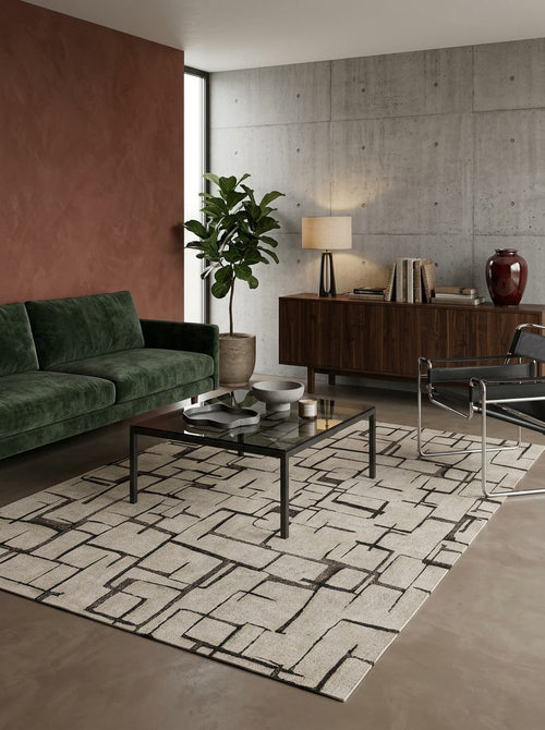 Load image 1 in gallery view. Cream rug with a black geometric grid pattern, styled in a modern living room with a green sofa and concrete walls.