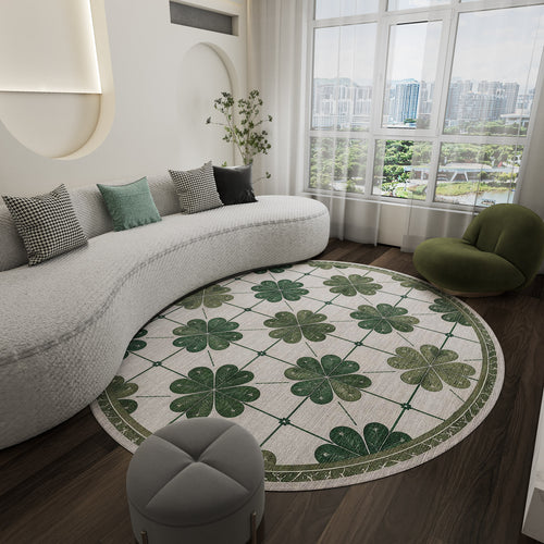 Load image 1 in gallery view. A modern living room featuring a curved white sofa, the Emerald Charm - Washable Rug - JRS013 with a green clover pattern for high-traffic areas, small gray ottoman, green lounge chair, and large window overlooking city buildings and trees.