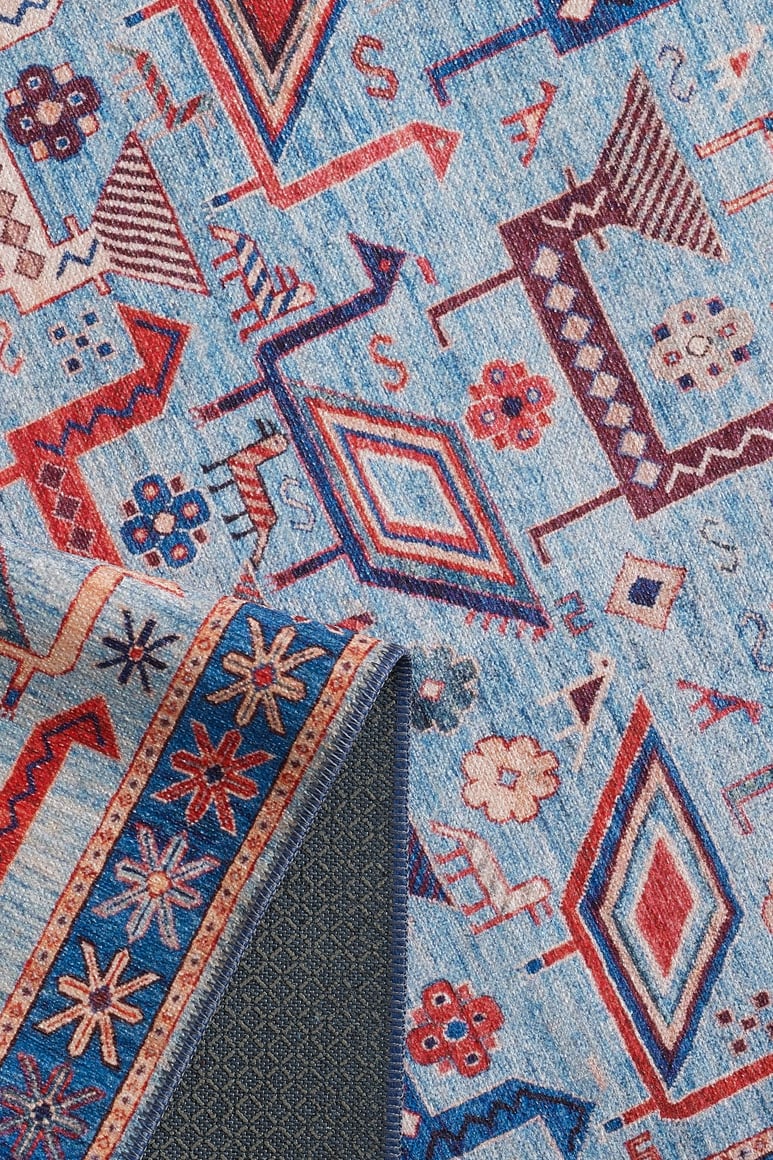 Close-up of the Birdwatcher's Dream Blue Washable Rug - LCC3020 (Custom Size) featuring colorful geometric and floral patterns in blue, red, and cream; a flipped corner reveals textured backing—perfect for high-traffic areas.