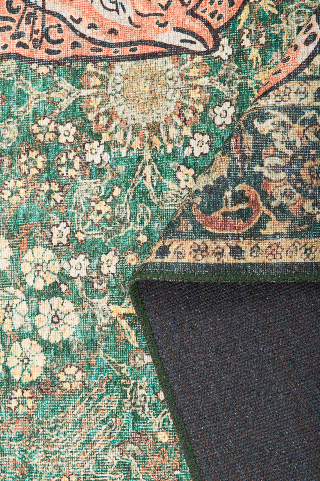 A close-up of the Jungle Ember - Washable Rug - JR0047, a colorful vintage-style green rug with cream and orange tones. One corner is folded to show the dark backing and detailed geometric front pattern.