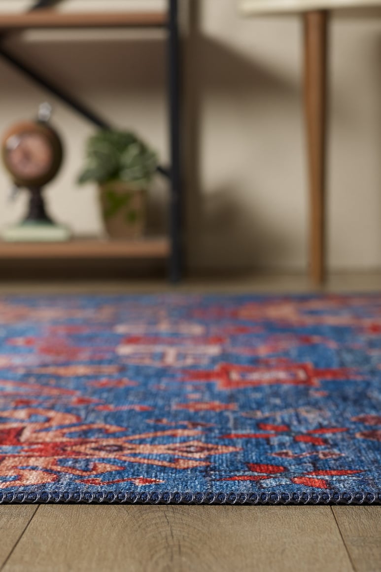 A close-up of the Kaleidos Authentic Blue Washable Rug - LCC3028 with red patterns on a wooden floor; in the background, a shelf with decor highlights this rug’s durability and suitability for high-traffic areas.