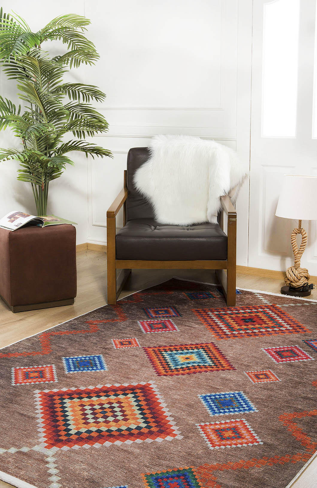 A modern living room with a brown armchair draped in a white faux fur throw, the Kilim Kingdom - Washable Rug - JR1536 (Custom Size) featuring vibrant geometric patterns, a small lamp, plant, and a brown ottoman topped with a magazine.