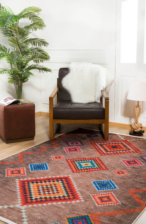 Bild 1 in Galerieansicht laden. A modern living room with a brown armchair draped in a white faux fur throw, the Kilim Kingdom - Washable Rug - JR1536 (Custom Size) featuring vibrant geometric patterns, a small lamp, plant, and a brown ottoman topped with a magazine.
