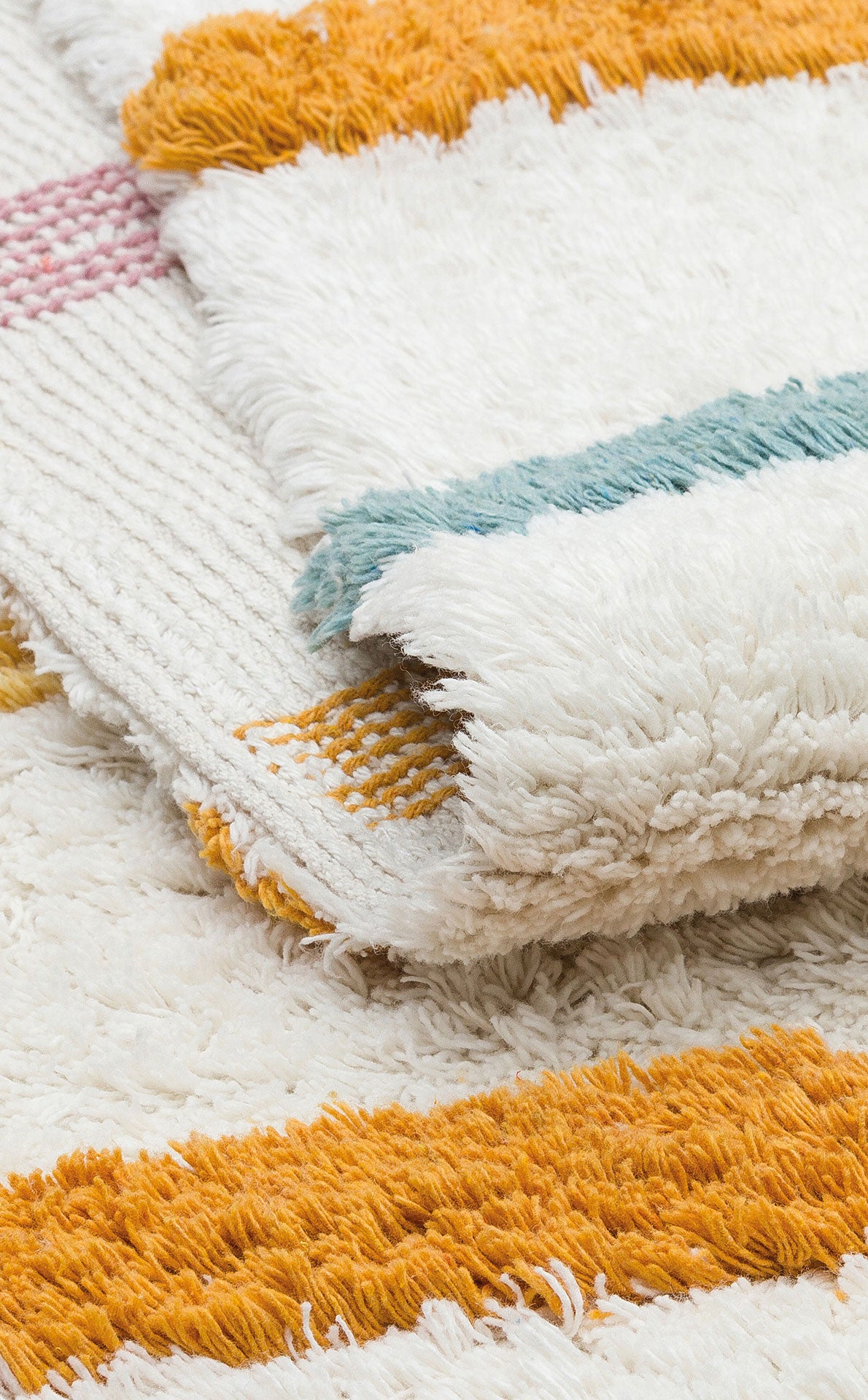 A close-up of the Little Steps - Washable Shaggy - CBN03 rugs, featuring vibrant orange, yellow, teal, and pink stripes with a fluffy textured surface, stacked together as a colorful multicolour set.