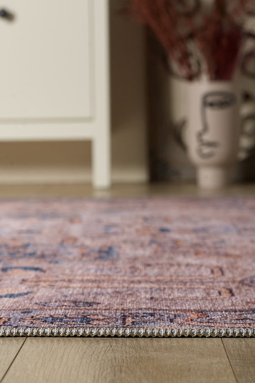 Load image 1 in gallery view. A close-up of the Luminary Beige Gray Washable Rug (LCC3023) on a wooden floor, with part of a white cabinet and a decorative vase with an abstract face design visible in the blurred background.