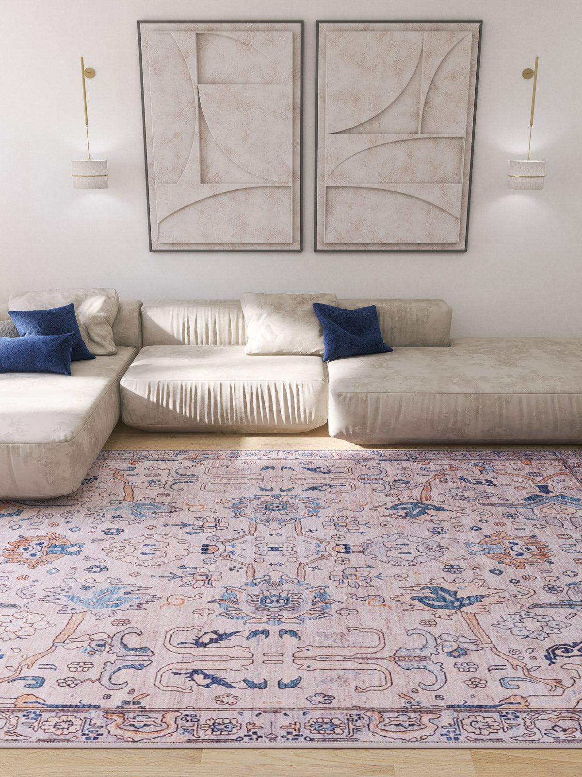 A bright living room with cream sofas, blue accent pillows, a Luminary Beige Gray Washable Rug - LCC3023 (Custom Size) for high-traffic areas, two abstract beige wall art pieces, and modern wall sconces.