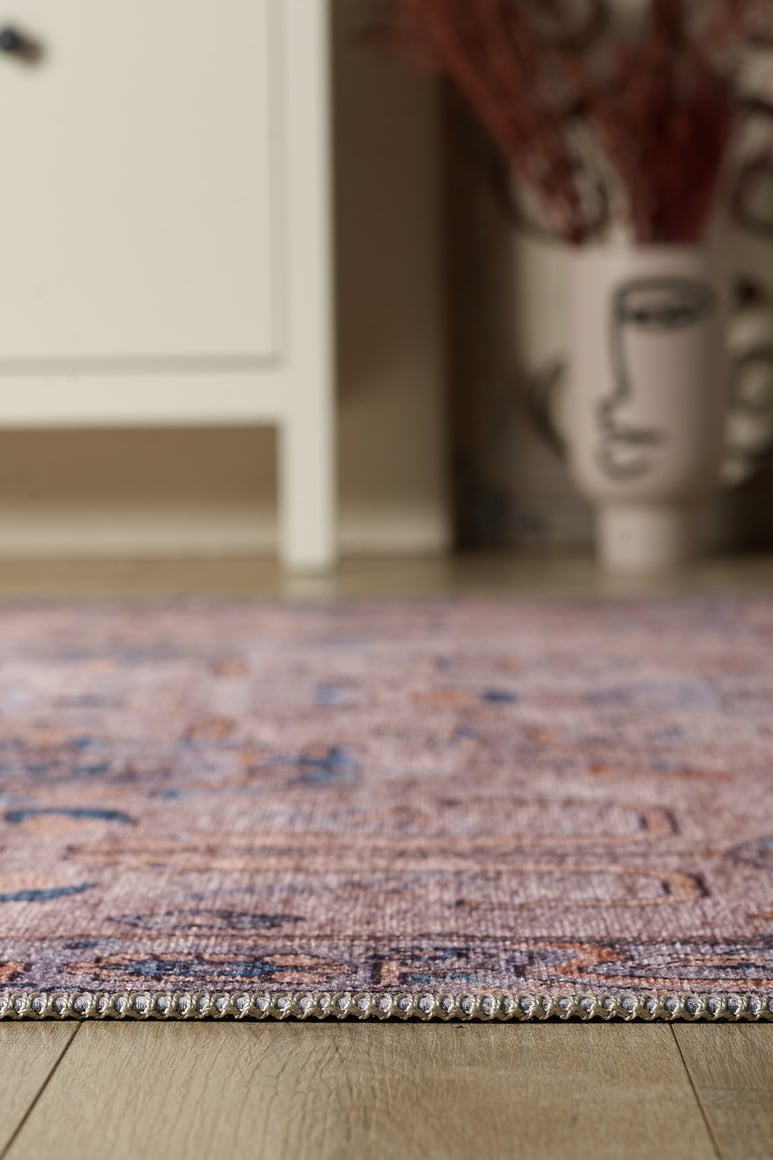A close-up of the Luminary Beige Gray Washable Rug (LCC3023 Custom Size) on a wooden floor, with a white cabinet and an abstract face vase with dried plants in the background—ideal for high-traffic spaces.