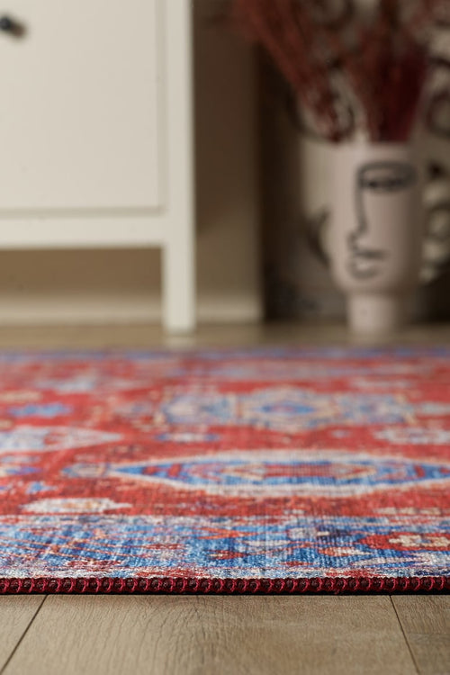 Load image 1 in gallery view. A close-up of the Lunavale Red Blue Washable Rug - LCC3007 (Custom Size) on a wooden floor, with a white cabinet and abstract face vase in the background—perfect for adding style and durability to high-traffic areas.