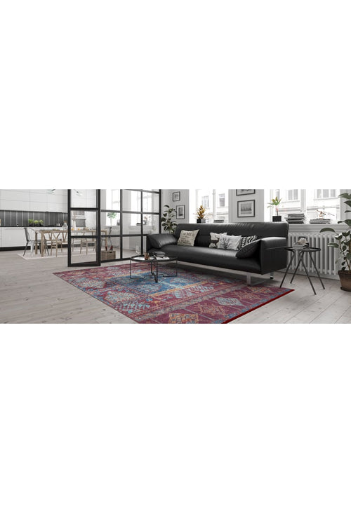 Load image 1 in gallery view. A modern living room features a black sofa, patterned cushions, a round coffee table, and the Majestic Mandarin - Washable Rug - JR1863 in colorful geometric patterns—ideal for busy spaces. Large windows provide natural light and a dining area is visible in the background.