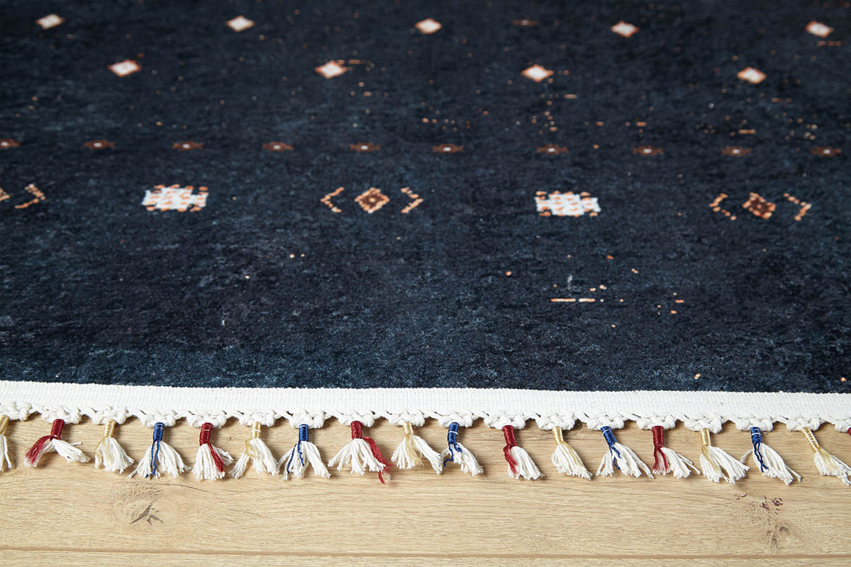 A close-up of the edge of the Midnight Majesty - Machine-Washable Rug - JRS5052 (Custom Size), featuring a dark blue pattern with tassels, resting on a light wooden floor—ideal for high-traffic areas.