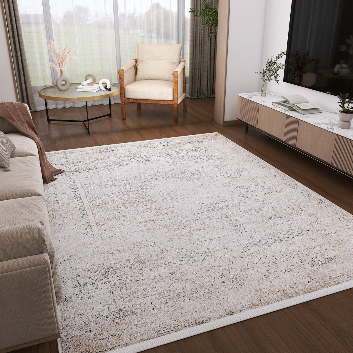 A modern living room features the Misty Mosaic - Washable Rug - JR1690 with a light pattern, paired with a beige sofa, wooden armchair, round decor coffee table, and a TV console accented by books, plants, and ample natural light from floor-to-ceiling windows.