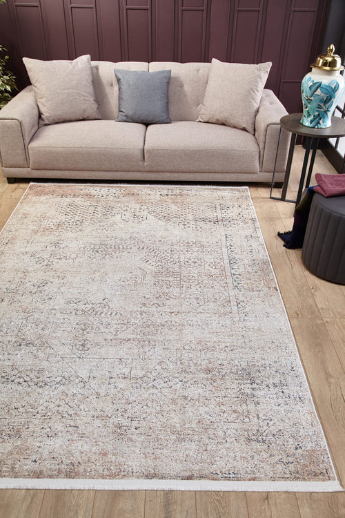 Load image 1 in gallery view. A beige sofa with three cushions sits against a dark mauve wall. On the wooden floor is the Misty Mosaic - Washable Rug - JR1690 (Custom Size), cream and beige in color, with a round side table and decorative jar on the right.