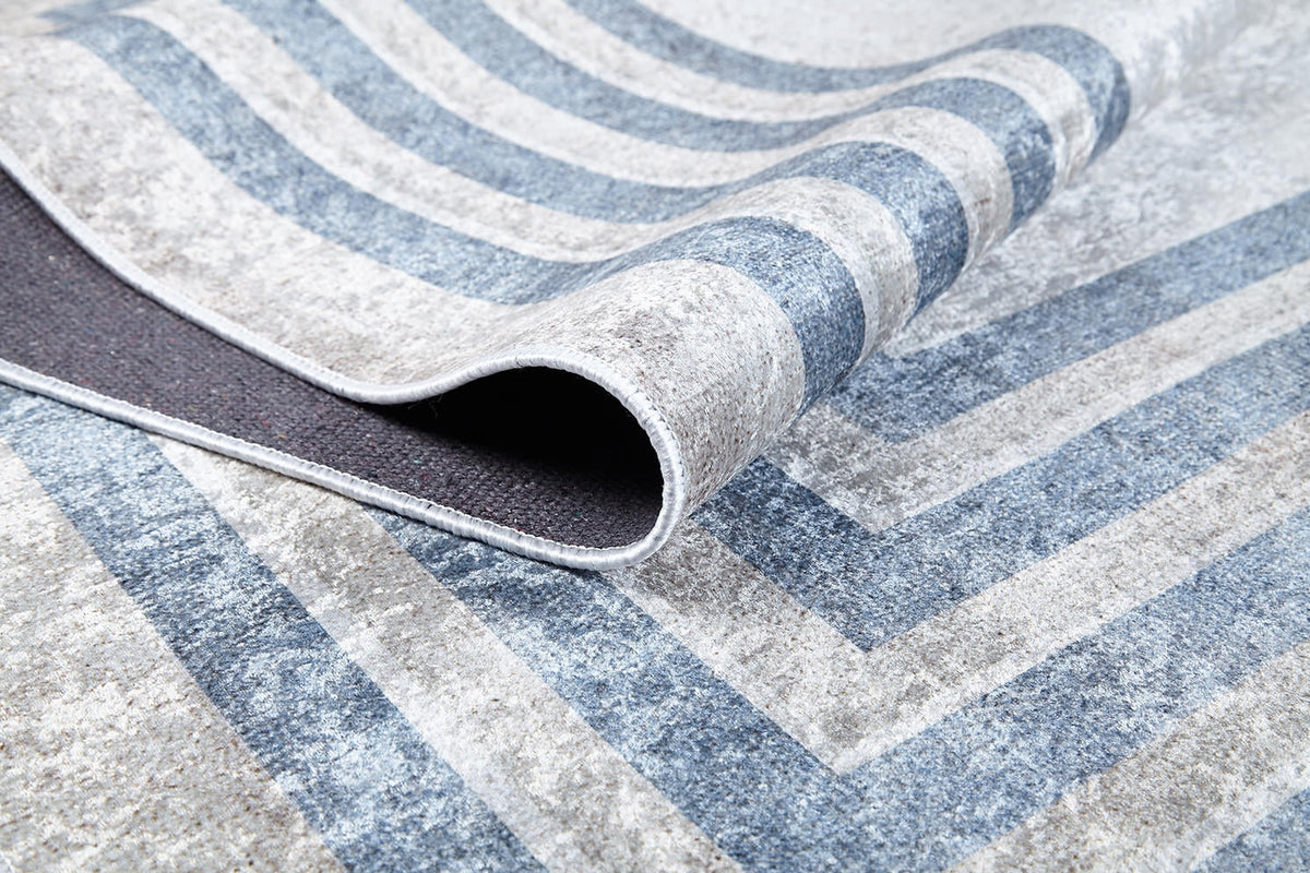 A close-up of the Modern and Regal - Washable Rug - JR1616 (Custom Size) in gray and blue stripes, with a corner folded to show its dark, textured non-slip backing—ideal for high-traffic areas.