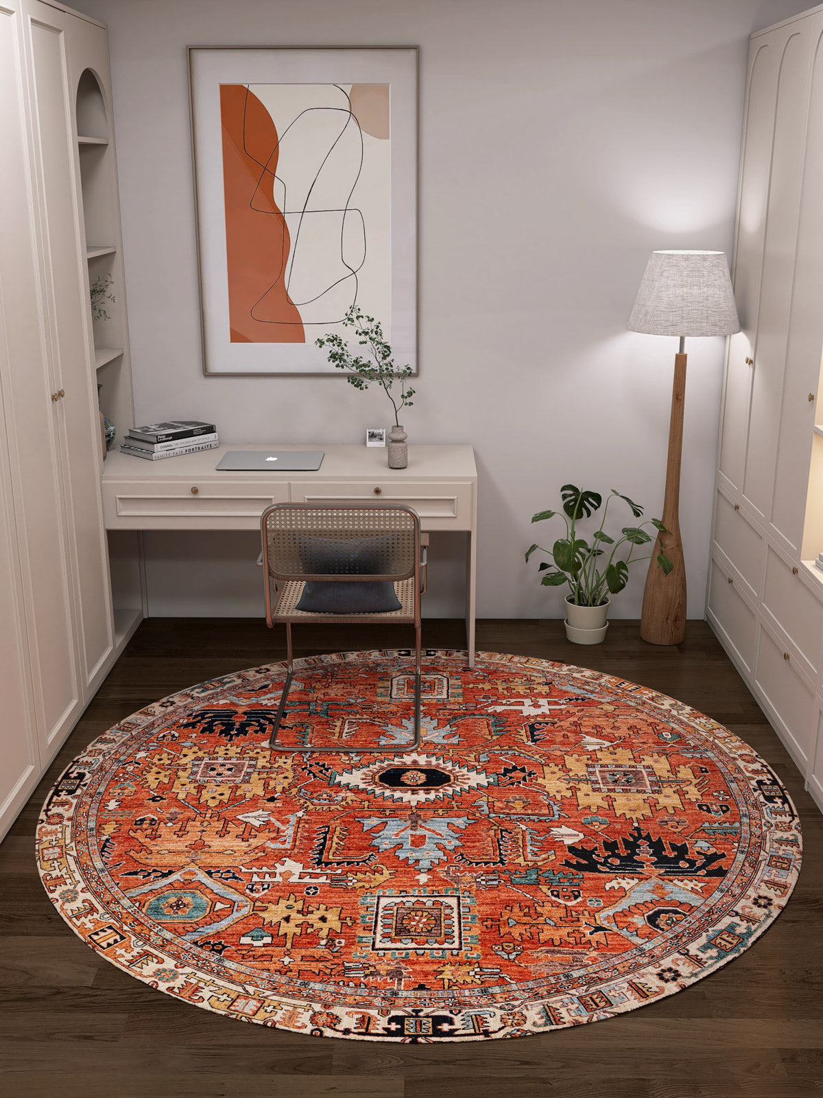 A cozy home office with a white desk, wicker chair, floor lamp, potted plant, abstract wall art, and the Mystral Kilim-Design Coral Washable Rug (LCC3015), featuring intricate patterns—ideal for high-traffic areas—over a dark wood floor.