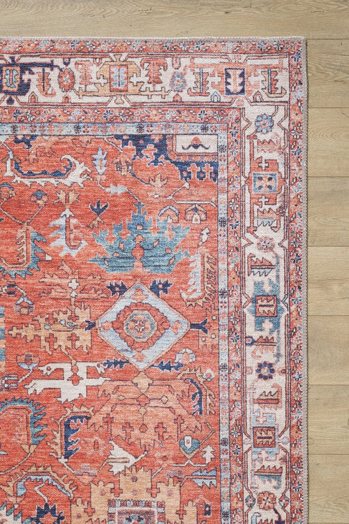 Load image 1 in gallery view. A close-up of the Mystral Kilim-Design Coral Washable Rug - LCC3015, showing its intricate red, blue, and cream geometric patterns—ideal for high-traffic areas. Only a corner of this colorful rug is visible on a light wooden floor.