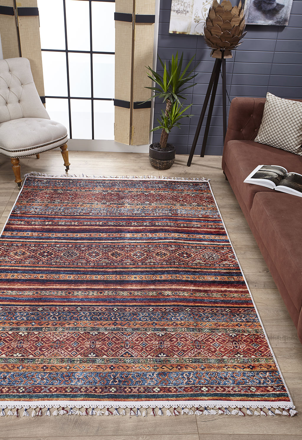 A living room featuring the Native Nightscape - Washable Rug - JR5093 (Custom Size) in multicolor on a wooden floor, paired with a brown sofa, beige tufted chair, potted plant, large windows with blinds, and décor against a gray wall. Perfect for high-traffic spaces.