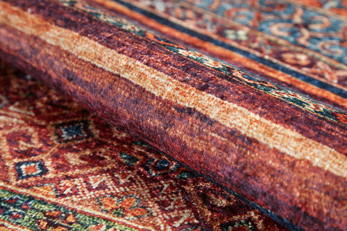 Load image 1 in gallery view. A close-up of the Native Nightscape - Washable Rug - JR5093 (Custom Size), featuring a folded section and intricate geometric patterns in rich red, orange, and brown tones.