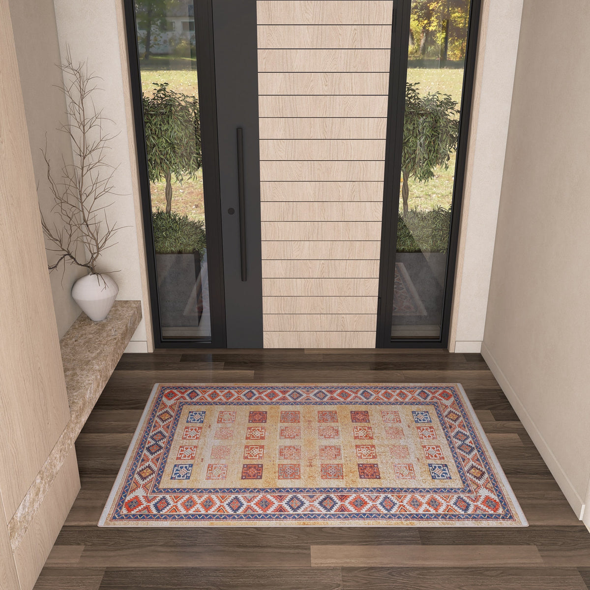 The Navajo Nights - Washable Rug - JR1758, with its colorful geometric pattern, decorates a modern entryway featuring light walls, a marble bench with a white vase and bare branches, and a large glass door—ideal for high-traffic areas.