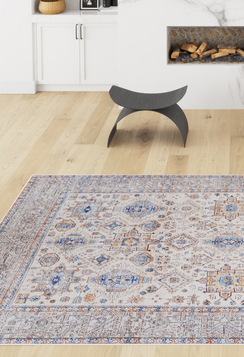 Load image 1 in gallery view. A modern living room with light wood floors, the Nexa Bordered Beige Washable Rug (LCC3009) featuring blue and orange accents, a black curved stool, fireplace with stacked logs, and white cabinets topped with a woven basket.