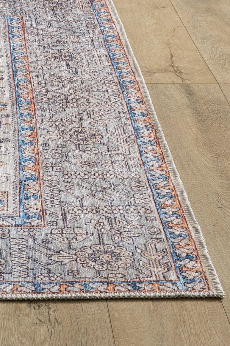 A close-up of the Nexa Bordered Beige Washable Rug (LCC3009) on a light wood floor. This flat weave rug features blue, orange, and beige tones with intricate floral and geometric designs, a decorative border, and easy maintenance.
