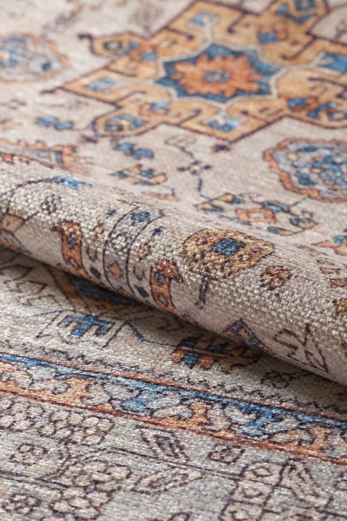 Load image 1 in gallery view. A close-up of the Nexa Bordered Beige Washable Rug - LCC3009 (Custom Size), showing intricate floral and geometric patterns in beige, blue, gold, and brown, with a folded edge highlighting its texture—ideal for high-traffic spaces.