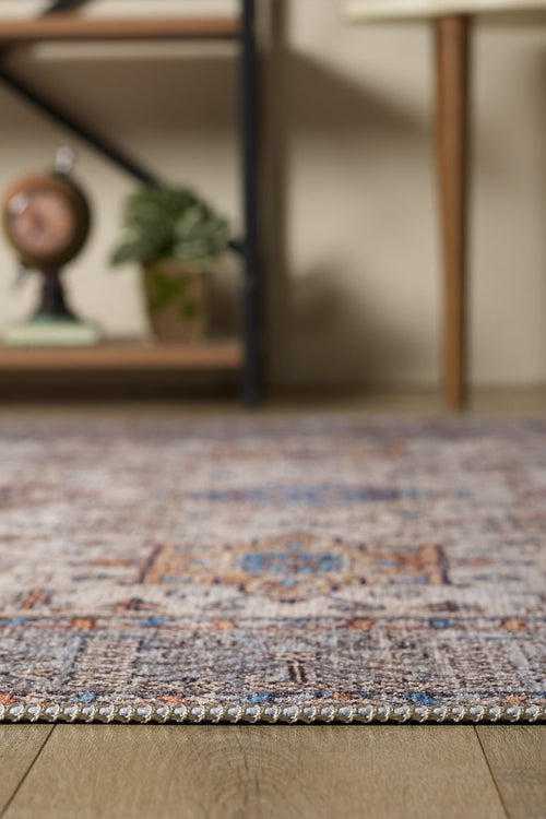 Load image 1 in gallery view. A close-up of the Nexa Bordered Beige Washable Rug - LCC3009 (Custom Size) on a wooden floor, ideal for high-traffic areas, with a shelf in the background holding a globe and potted plant, plus part of a table with wooden legs.