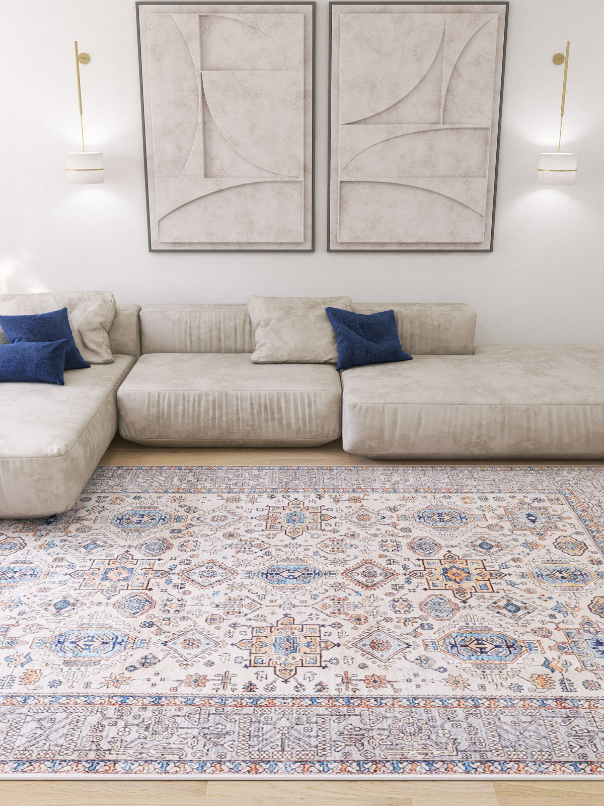 A modern living room with a light beige sectional sofa, blue accent pillows, abstract wall art, two wall-mounted lamps, and the Nexa Bordered Beige Washable Rug - LCC3009 (Custom Size)—ideal for high-traffic areas.
