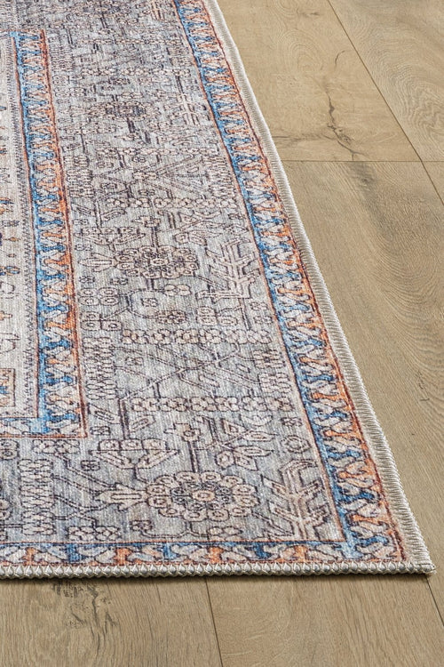 Load image 1 in gallery view. A close-up of the Nexa Bordered Beige Washable Rug - LCC3009 (Custom Size) shows its intricate floral and geometric patterns in blue, gray, and beige with orange-accented borders, laid on a light wood floor—perfect for high-traffic areas.