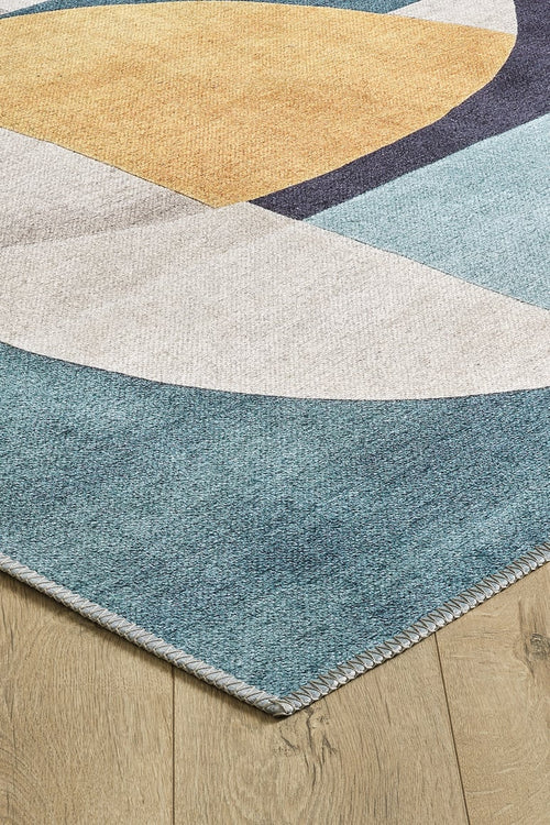 Load image 1 in gallery view. A close-up of the Nexus Geometric Contemporary Washable Rug - MDJ006, featuring blue, beige, gold, and white geometric shapes on a light wood floor. This rug has stitched edges, a modern abstract design, and is ideal for high-traffic areas.