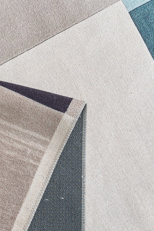 Load image 1 in gallery view. Close-up of the Nexus Geometric Contemporary Washable Rug - MDJ006, featuring overlapping beige, cream, blue, and gray shapes. Its flipped corner shows the textured underside—perfect for allergy-sensitive homes and high-traffic spaces.