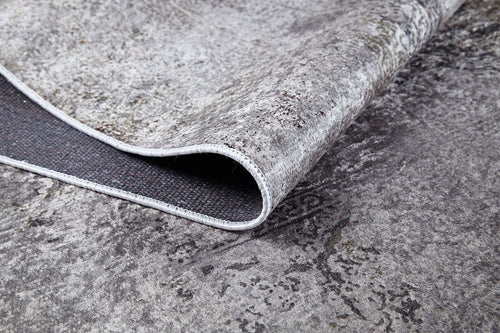 Bild 1 in Galerieansicht laden. A close-up of the Noble Insignia - Washable Rug - JR1830 (Custom Size) in textured grey, with a corner lifted to show its dark backing and stitched edge—perfect for high-traffic areas and blending seamlessly with similar colored floors.