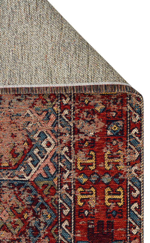 Load image 1 in gallery view. Close-up of a corner of the Nomad Spirit - Washable Kilims - AND03 rug, featuring geometric and floral patterns in red, blue, gold, and cream, with its underside folded to reveal the textured backing.