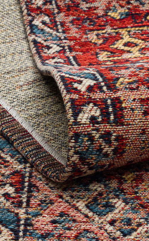 Load image 1 in gallery view. A close-up of the Nomad Spirit - Washable Kilims - AND03 rug highlights its intricate red, blue, and cream flatwoven patterns, with the edge folded to showcase the detailed texture and reversible design