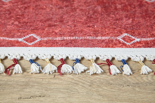 Load image 1 in gallery view. A close-up of the Nomadic Journey - Washable Rug - JR5080 (Custom Size), featuring red and white geometric designs, a tasseled fringe, plus blue and red threads—ideal for high-traffic areas on light wood flooring.