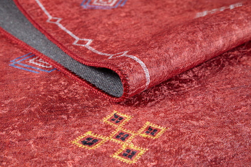 Load image 1 in gallery view. A close-up of the Nomadic Journey - Washable Rug - JR5080 (Custom Size) shows red geometric patterns in yellow, blue, and white. The partially folded rug reveals a grey underside and stitched edge—ideal for high-traffic spaces.