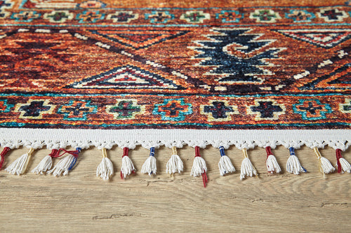 Load image 1 in gallery view. Close-up of the edge of the Nomadic Oasis - Washable Rug - JR5086 (Custom Size), featuring colorful geometric patterns, white fringe tassels with red and blue thread, ideal for high-traffic areas, shown on a wooden floor.