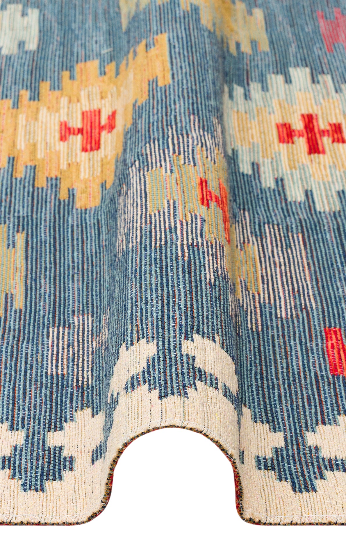A close-up of the Ocean Form - Washable Reversible Kilim (NMD04) in blue with cream, red, and yellow geometric patterns. The rug curves upward in the middle, showcasing its textured weave and vibrant design.