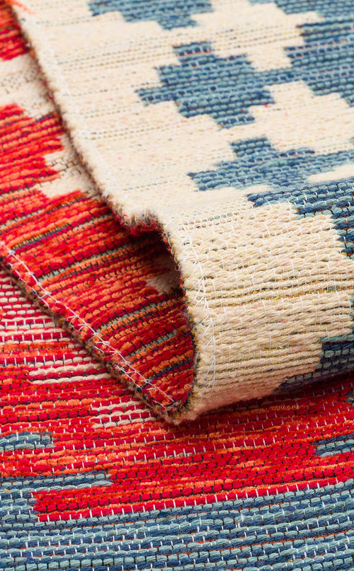 Bild 1 in Galerieansicht laden. A close-up of the Ocean Form - Washable Reversible Kilim - NMD04 shows its folded corner, revealing red, blue, and beige geometric patterns and textured stitching on the back.