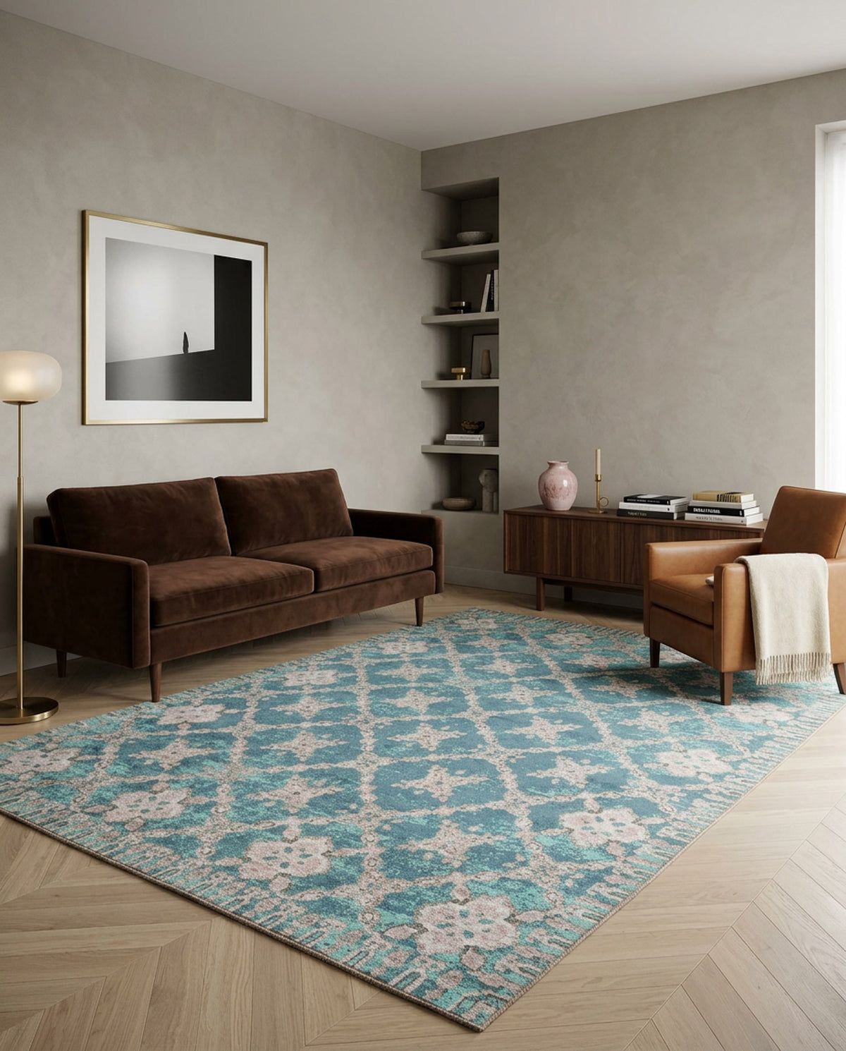 A modern living room with a brown sofa, tan armchair, wooden cabinet, and the Ocean Trellis Area Rug APX1942. A floor lamp, vase, books, abstract wall art, and built-in shelves complete the space as sunlight enters from a window on the right.