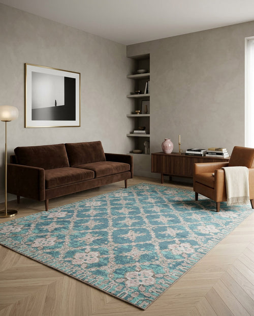 Load image 1 in gallery view. A modern living room with a brown sofa, tan armchair, wooden cabinet, and the Ocean Trellis Area Rug APX1942. A floor lamp, vase, books, abstract wall art, and built-in shelves complete the space as sunlight enters from a window on the right.