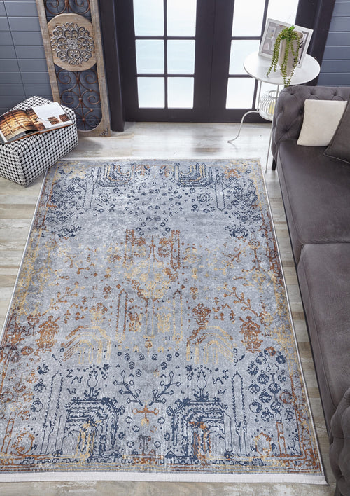 Bild 1 in Galerieansicht laden. An Oriental Treasures - Machine-Washable Rug JR1613 (Custom Size) with blue, gold, and beige patterns is placed on a light wood floor by a gray sofa, checkered ottoman, and round table with a plant near glass doors.