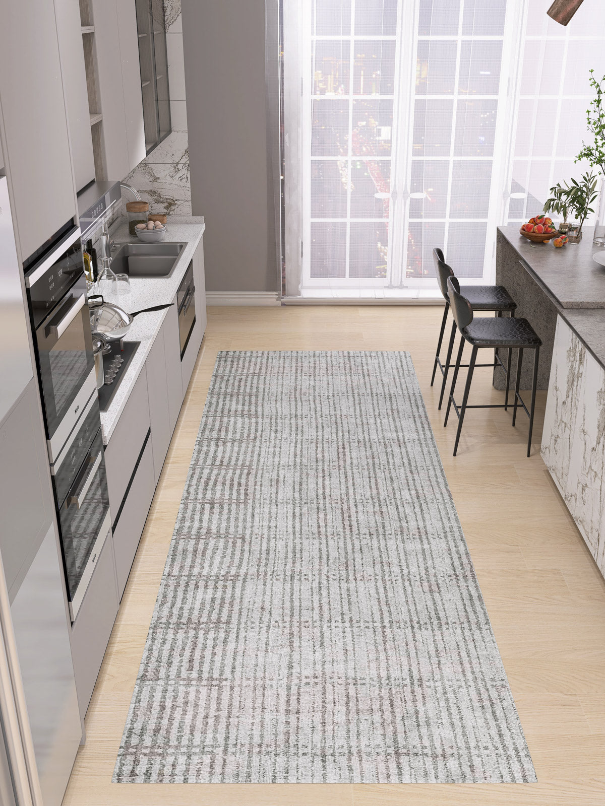Modern kitchen with light wood flooring, gray cabinets, built-in appliances, marble countertop, two bar stools, and the Ornate Hues - Washable Rug - JRN38—ideal for high-traffic areas. Large windows reveal a stunning cityscape view.