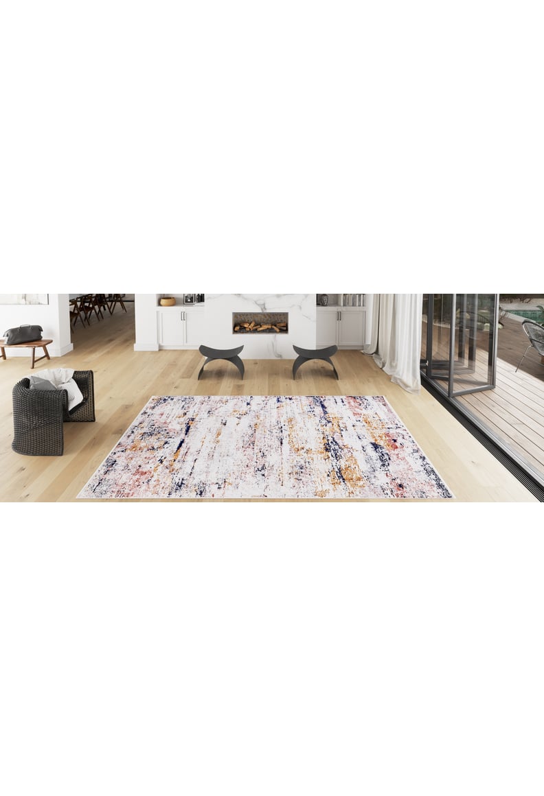 A modern living room with light wood floors, the Painted Dreams - Washable Rug - JR432 for high-traffic areas, a gray armchair, fireplace, two black stools, white cabinets, and large glass doors opening to a patio.