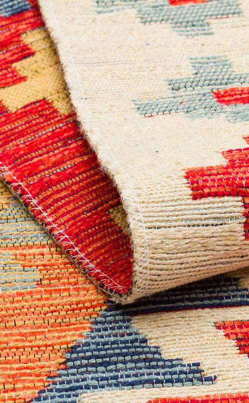 Load image 1 in gallery view. A close-up of the Pastel Grid - Washable Reversible Kilim (NMD09) rug shows its geometric patterns in red, beige, blue, and orange. A folded corner highlights the textured weave and stitching details of this washable kilim.